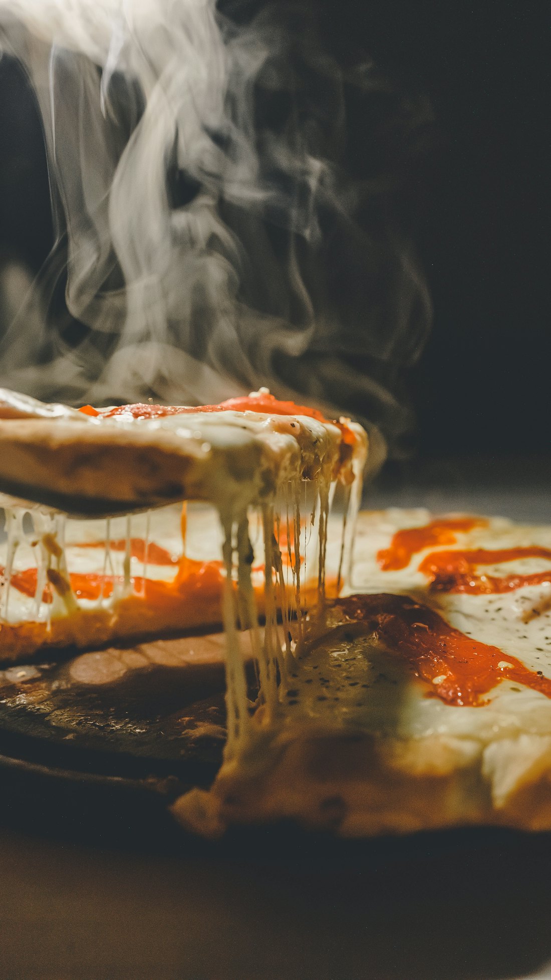 A wood-fired pizza slice lifted with a cheese pull
